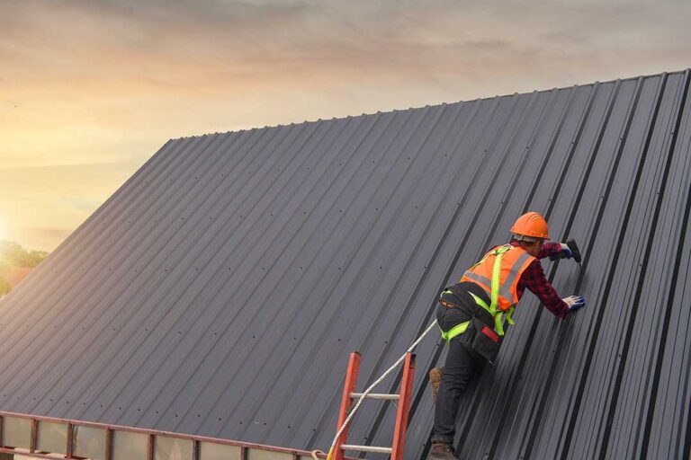A worker applies white roof coating to a flat building rooftop using a roller on a bright day.